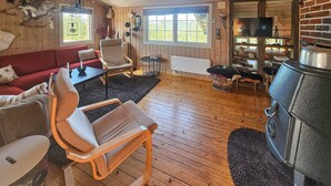 Ein gemütliches Blockhaus-Interieur mit Holzboden, einem roten Sofa, einem Holzstuhl, einem Kamin und einem Fernseher.