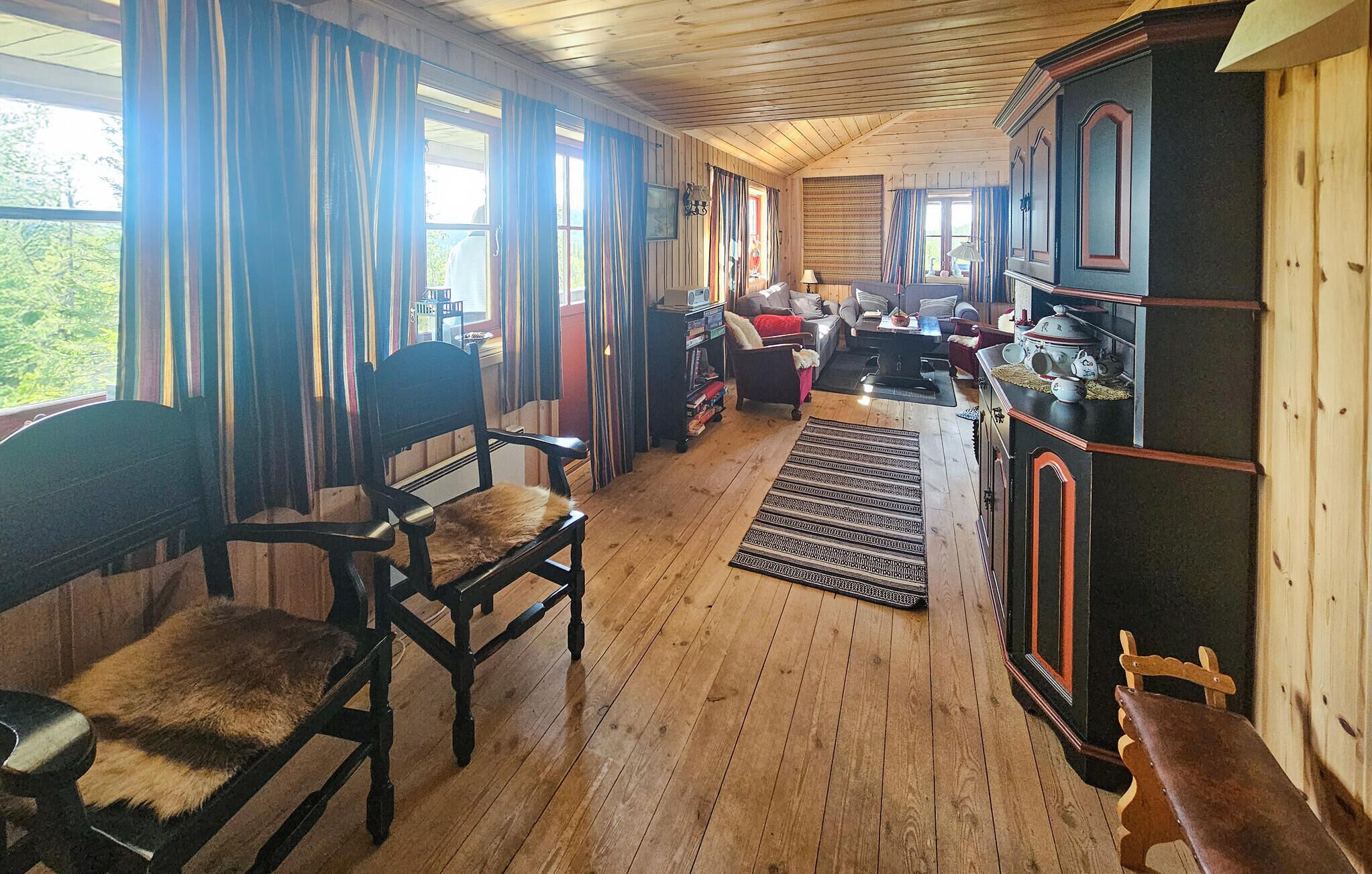 A cozy room with wooden floors, a fireplace, a dining area with a table and chairs, and a large window with curtains.