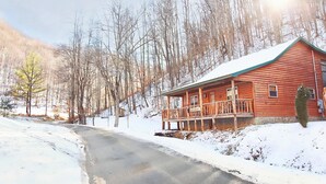 Una baita di legno con un portico, circondata da terreno e alberi innevati.