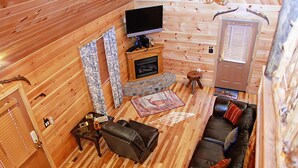 Un accogliente interno di una baita con camino, divano in pelle e televisore a schermo piatto.