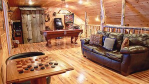 Una stanza accogliente con soffitto in legno, tavolo da biliardo, divano in pelle e tavolino in legno con una scacchiera.