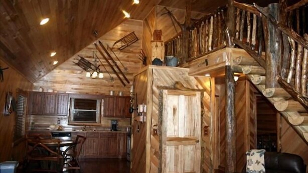 Interior rústico de una cabaña con escalera de madera, una zona de cocina y un comedor.