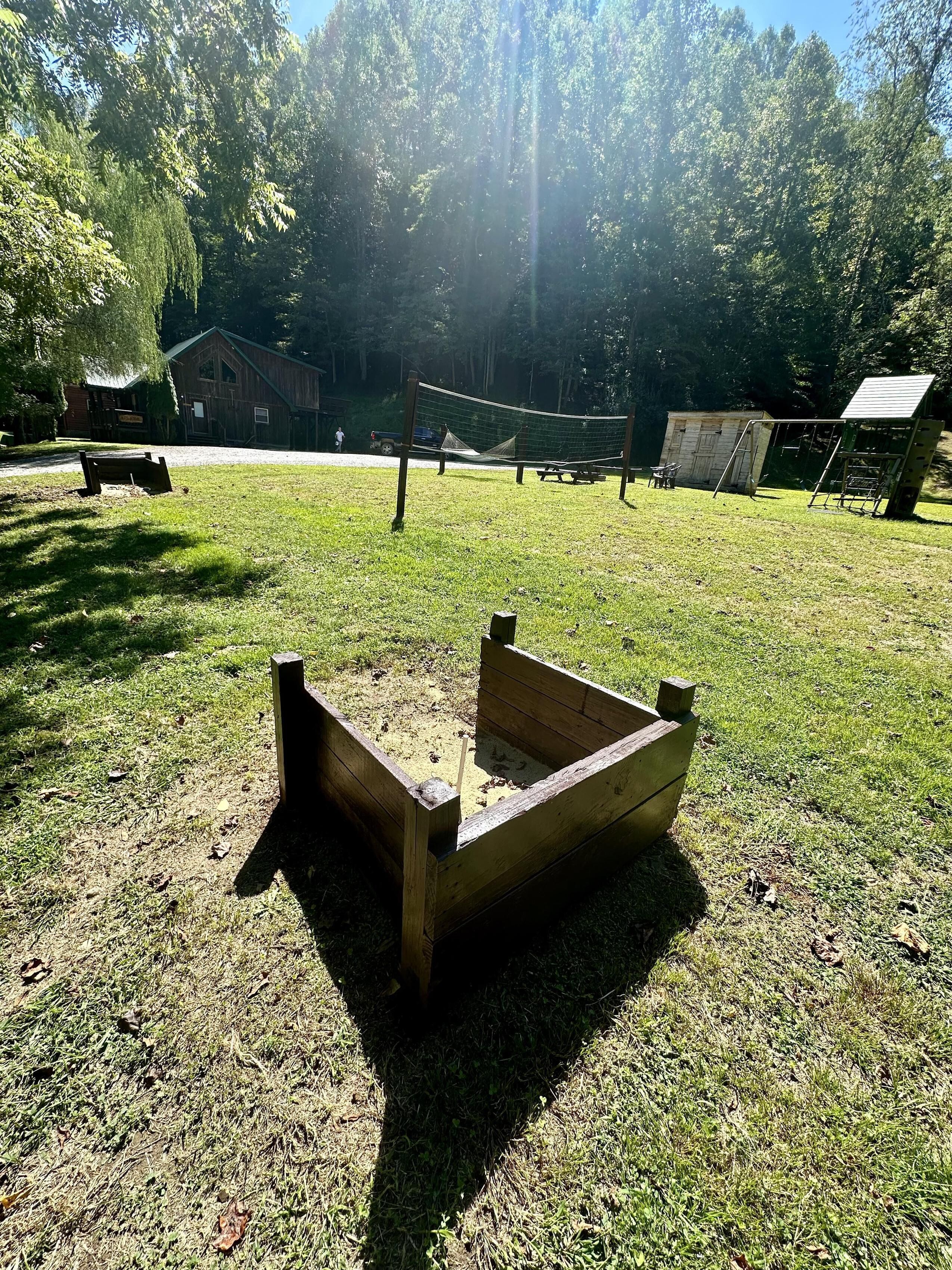 Een houten speelconstructie in een grasrijk gebied, met een picknicktafel en een klein tuinhuisje op de achtergrond.
