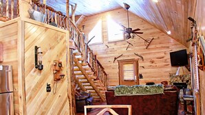 Interior de una cabaña de troncos con escalera de madera, un área de cocina y una zona de estar.