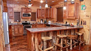A rustic kitchen with wooden cabinets, a central island with stools, a refrigerator, and a microwave. - 3-Bedroom Master Deluxe (Chapmanville)
