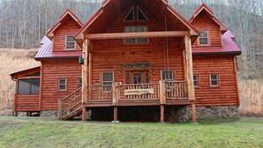 A log cabin with a porch, a staircase, and a sign that reads "HillBilly Hilton." - 3-Bedroom Master Deluxe (Chapmanville)