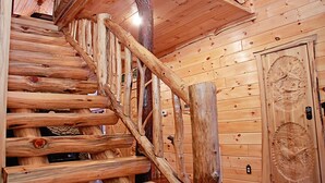 A wooden staircase with a rustic design, a wooden door with intricate carvings, and a ceiling with wooden beams. - 3-Bedroom Master Deluxe (Chapmanville)