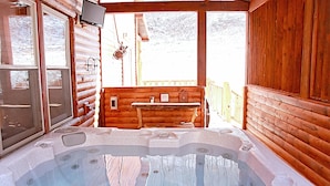 Eine Holzhütte mit Whirlpool, Holzwänden und einem Fenster mit Blick auf eine verschneite Landschaft.