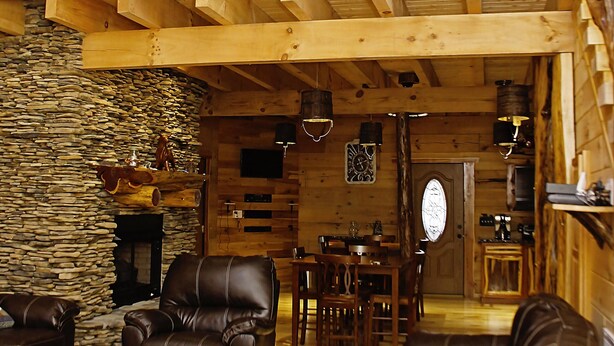 Ein rustikaler Holzinnenraum mit Steinwand, Ledermöbeln und einem Holzbalkon.