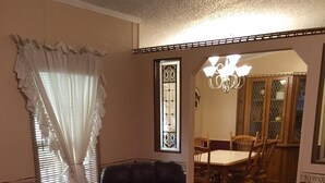 A living room with a leather armchair, a wooden table, and a dining area with a chandelier. - Creek Side Retreat (Chapmanville)