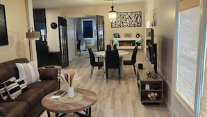 Ein modernes Wohnzimmer mit braunem Sofa, einem Couchtisch und einem Essbereich mit einer Pendelleuchte.