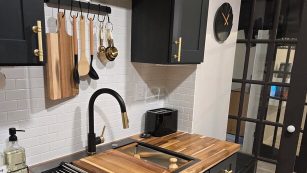 Eine moderne Küche mit schwarzen Schränken, einer Holzarbeitsplatte, einem schwarzen Wasserhahn und einem schwarzen Toaster.