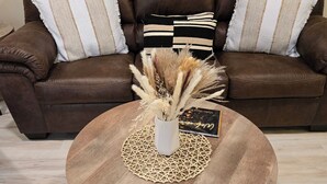 Ein braunes Ledersofa mit gestreiften Kissen, ein runder Couchtisch mit einer gewebten Unterlage und eine Vase mit Trockenpflanzen.