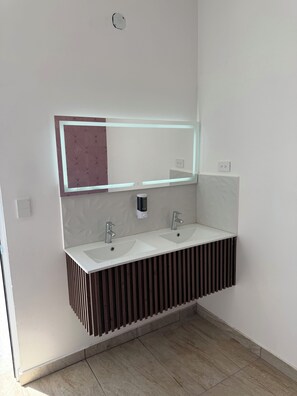 A modern bathroom with a dual sink vanity, a wall-mounted mirror with integrated lighting, and a wooden panel design.