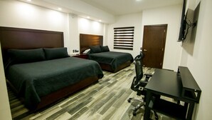 Ein Hotelzimmer mit zwei Betten, einem Schreibtisch, einem Stuhl, einem an der Wand befestigten Fernseher und einem Fenster mit Jalousien.