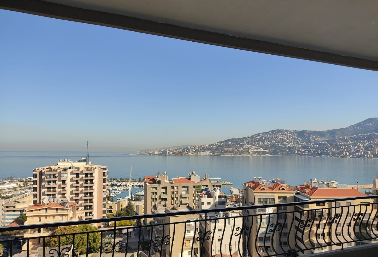 A balcony with a view of a coastal cityscape, including buildings and a body of water.