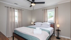 Uma cama bem arrumada com um edredom branco e azul-turquesa, uma mesa de cabeceira com abajur e um ventilador de teto.