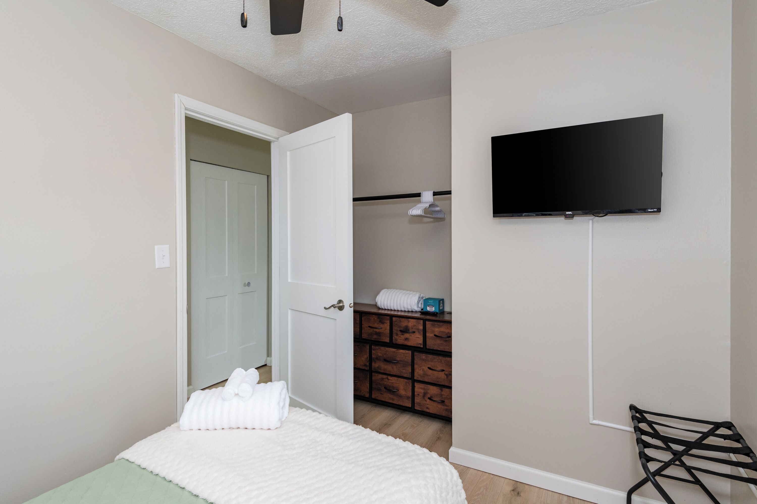 Une chambre avec un lit, un téléviseur fixé au mur, une porte donnant sur une salle de bain et une petite table avec une chaise.