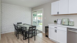 Cozinha moderna com armários brancos, uma mesa de jantar com cadeiras e um forno embutido.