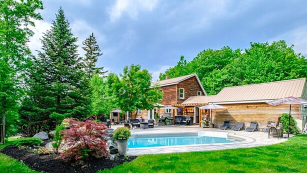 Un patio trasero con piscina, terraza de madera y zona de estar exterior.