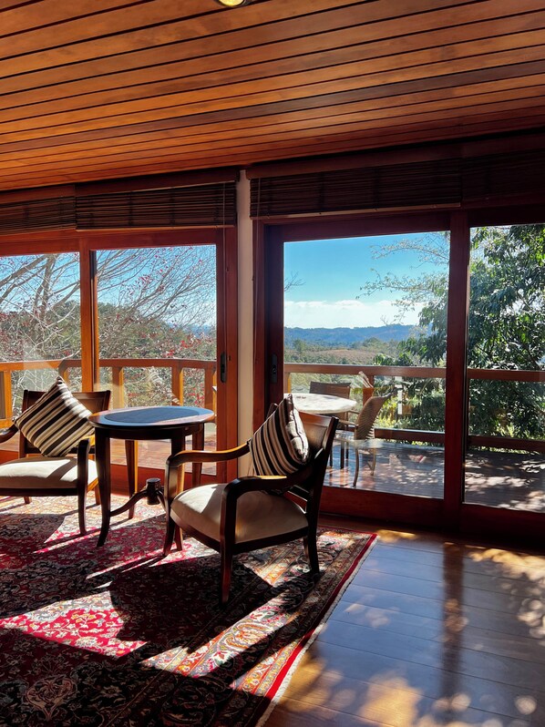A room with a wooden ceiling, large windows, a wooden deck, and a view of the outdoors.