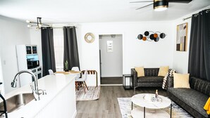 Ein modernes Wohnzimmer mit Sofa, Couchtisch und Essbereich mit weißer Arbeitsplatte und Stühlen.