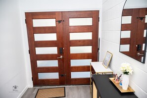 Eine Holztür mit Fensterfeldern, ein kleiner Tisch mit Blumenvase und ein gerahmtes Bild an der Wand.