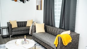 Ein modernes Wohnzimmer mit einem grauen Sofa, zwei Sesseln, einem Couchtisch und einem gemusterten Teppich.