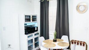 Ein modernes Zimmer mit einem weißen Schrank, einem runden Tisch mit vier Stühlen, einer Topfpflanze und einer Wanduhr.