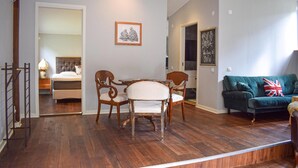 A room with a wooden floor, a dining table with chairs, a sofa, a bed, and a framed picture on the wall.