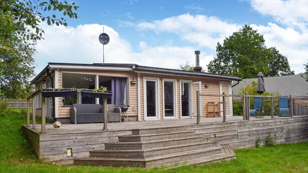 A wooden house with a covered porch, a satellite dish, and a grill area.