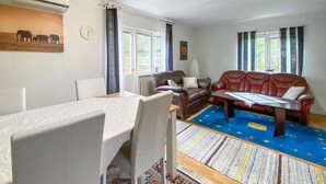Een woonkamer met een bruine leren bank, een eettafel met stoelen en een kamerkleed met een patroon.