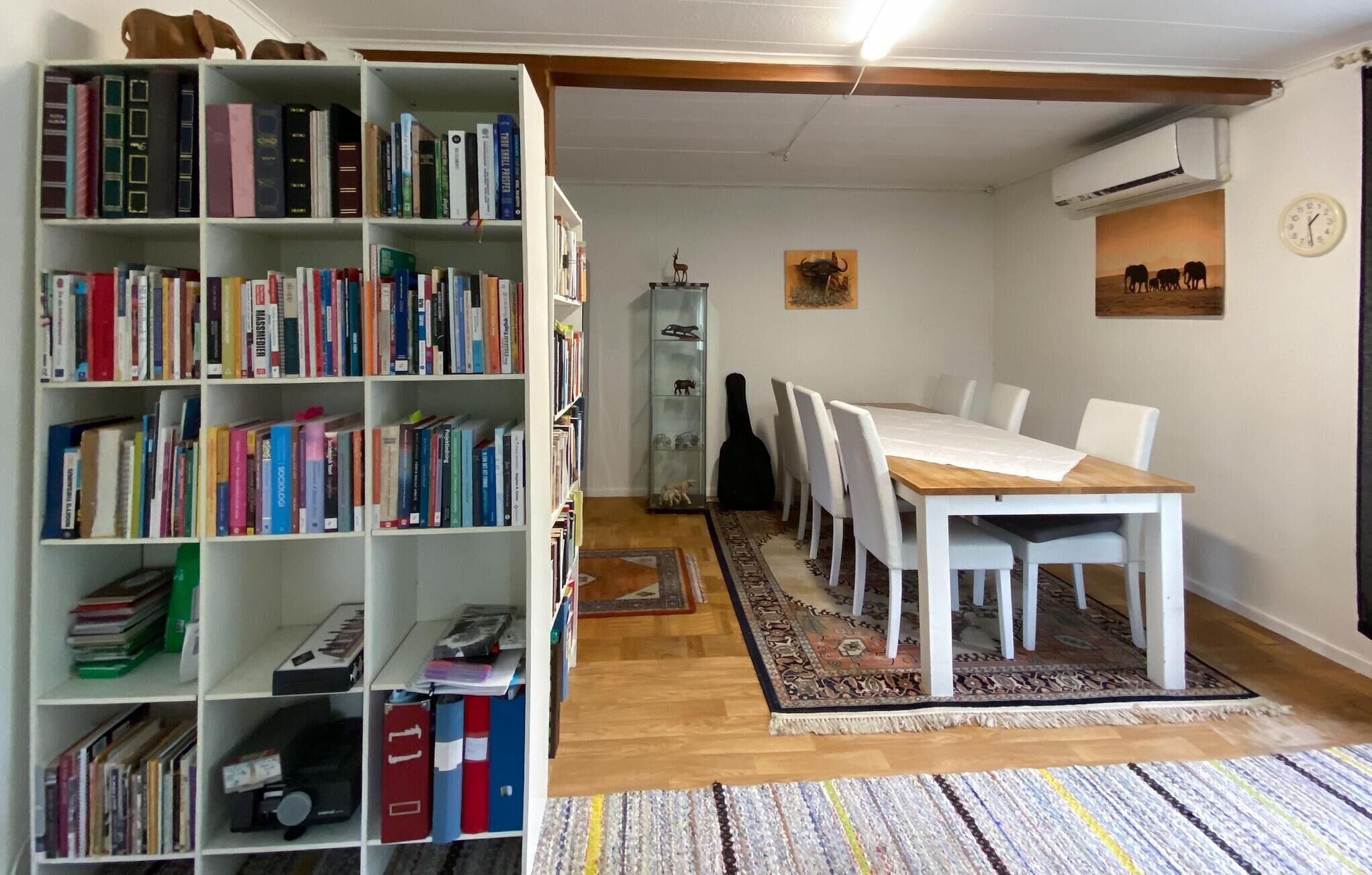 Huone, jossa on ruokapöytä, tuoleja, kirjahylly ja matto.