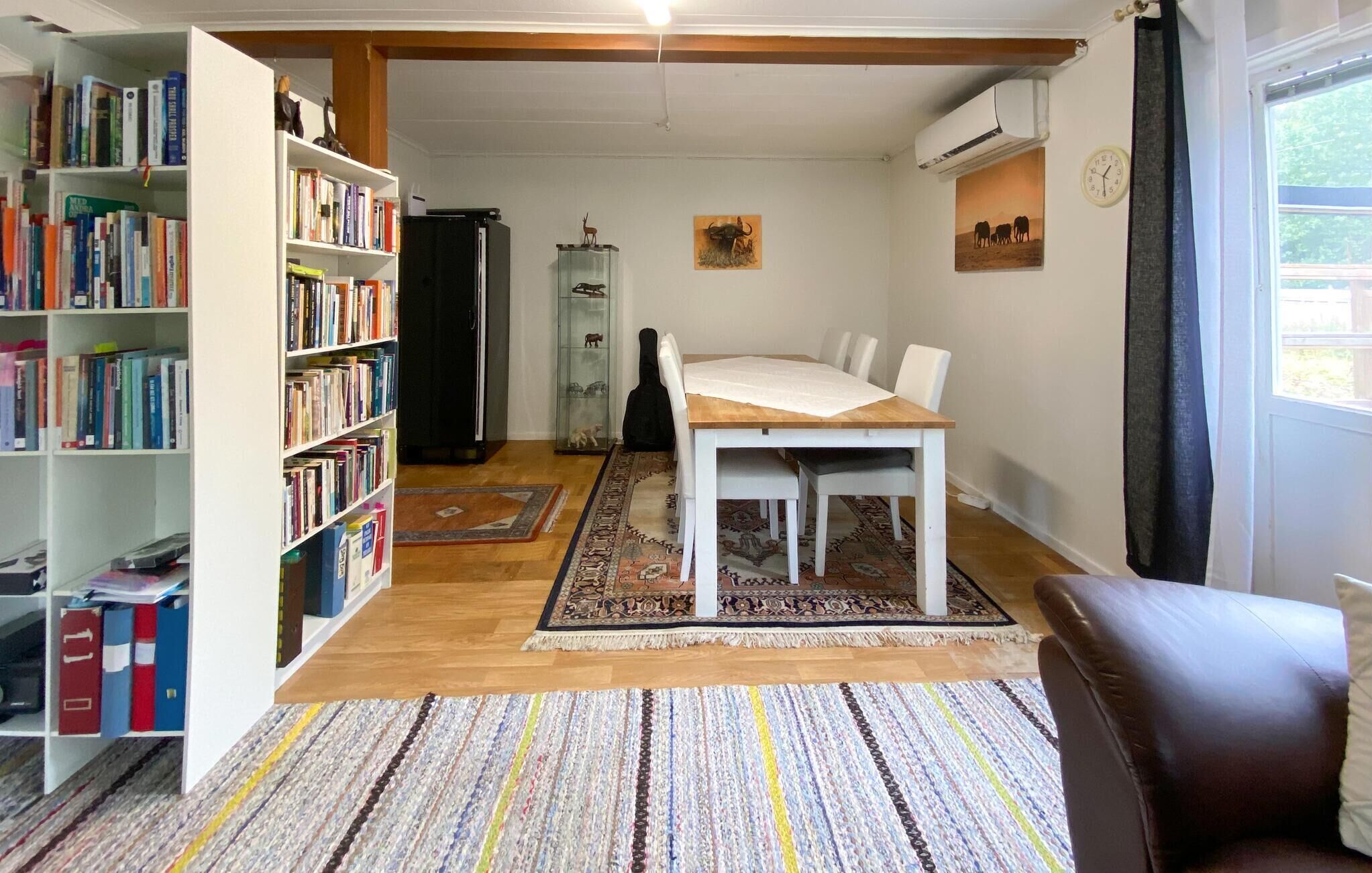 A cozy living room with a dining table, a bookshelf filled with books, a guitar, and a patterned rug.