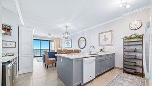 A modern kitchen with grey cabinets, a white island, and a large window. - Grand Pointe 306 | Beachfront, Pools, Saunas, Hot Tub | My Beach Getaways (Orange Beach)