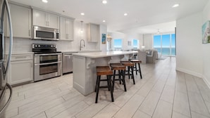 A modern kitchen with stainless steel appliances, a large island with bar stools, and a view to the outside. - Spanish Key 301 | Steps from Flora Bama | Pools, Hot Tub | My Beach Getaways (Pensacola)