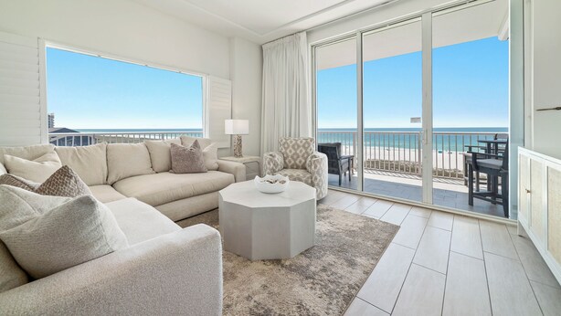 A spacious living room with a large sofa, a round coffee table, and a view of the beach through large sliding doors. - Spanish Key 301 | Steps from Flora Bama | Pools, Hot Tub | My Beach Getaways (Pensacola)