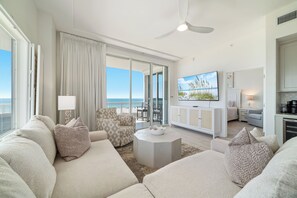 A modern living room with a sofa, armchair, and coffee table, a flat-screen TV, and a view of the ocean.