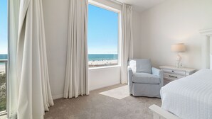 A hotel room with a large window, a bed, a chair, a nightstand, and a lamp. - Spanish Key 301 | Steps from Flora Bama | Pools, Hot Tub | My Beach Getaways (Pensacola)