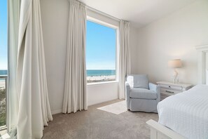 A hotel room with a large window, a bed, a chair, a nightstand, and a lamp. - Spanish Key 301 | Steps from Flora Bama | Pools, Hot Tub | My Beach Getaways (Pensacola)