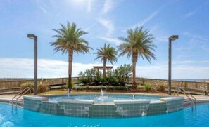 A swimming pool with a central fountain, surrounded by palm trees and a wooden deck.