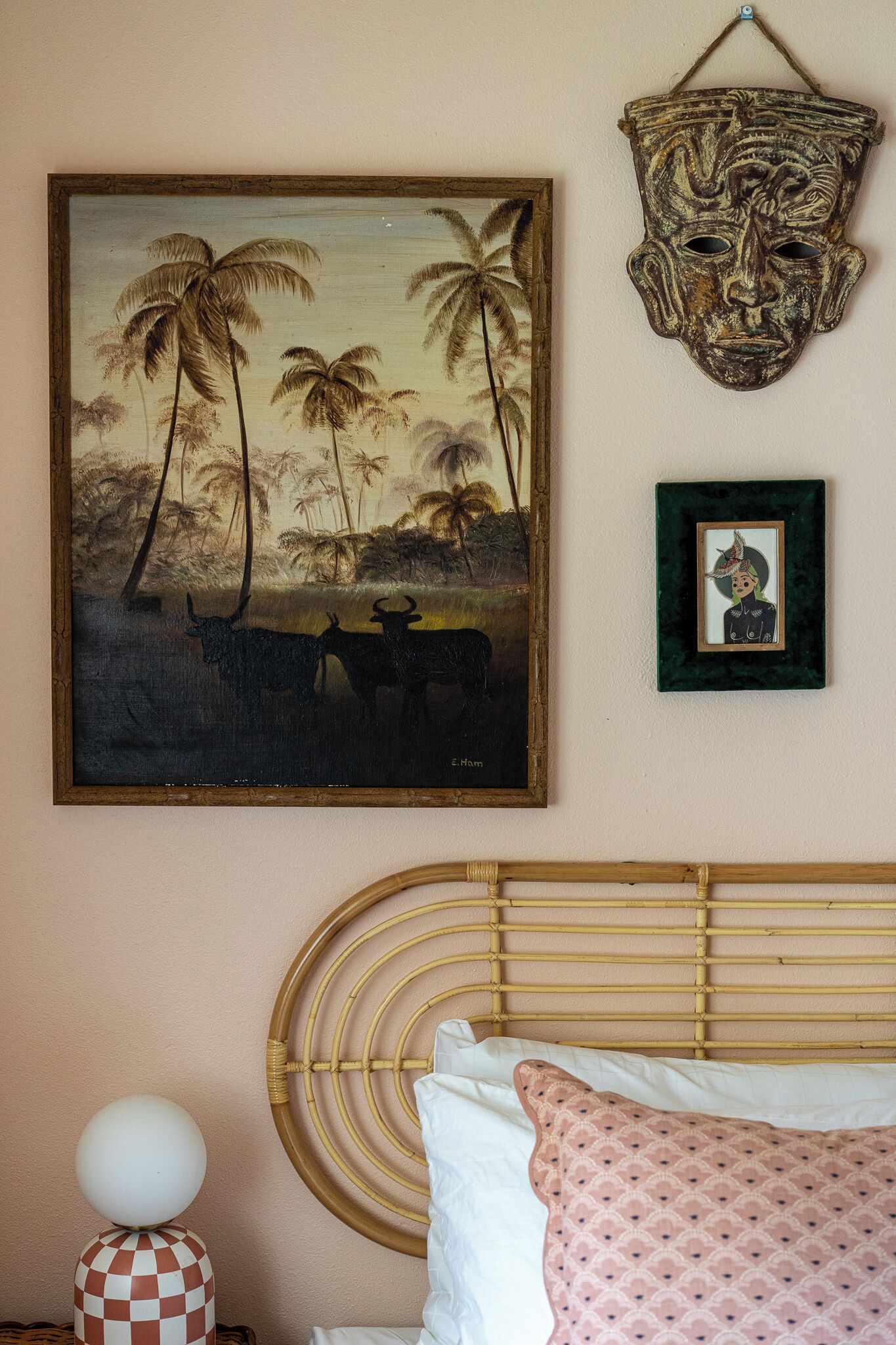 A bedroom with a bed, a wall-mounted headboard, a framed painting, and a decorative mask.