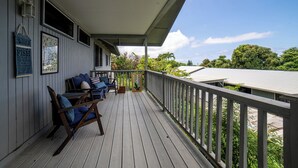 A wooden deck with a railing, a covered seating area with blue cushions, and a view of the surrounding greenery.