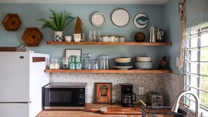 A kitchen with wooden shelves, a microwave, a coffee maker, and a toaster.