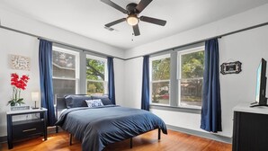 A bedroom with a bed, a nightstand, a desk, a ceiling fan, and large windows with curtains. - *Mins To Methodist Hospital* Lux & Cozy* (San Antonio)