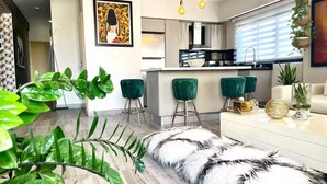 A modern kitchen with a central island, green bar stools, and a white sofa with a fluffy rug. - NewExclusive Apartment Downtown, GYM, POOL&MORE 407 (Santo Domingo)