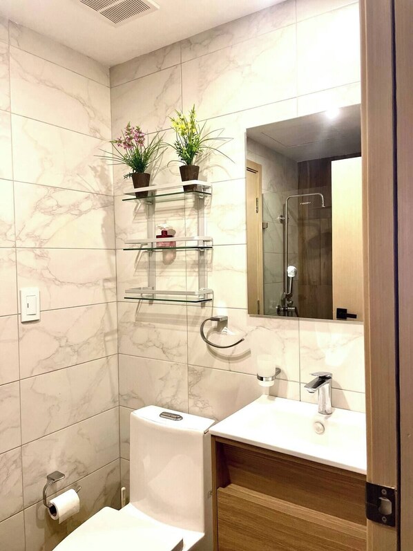 A modern bathroom with marble tiles, a toilet, a sink with a mirror, and two shelves with plants. - New, exclusive apartment in the city center, gym, pool, and more 407 (Santo Domingo)