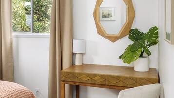 A bedroom with a bed, a desk, a chair, a potted plant, and a window with curtains.