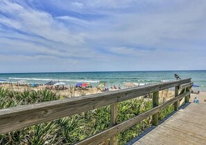 A wooden boardwalk leading to a beach with umbrellas and people.