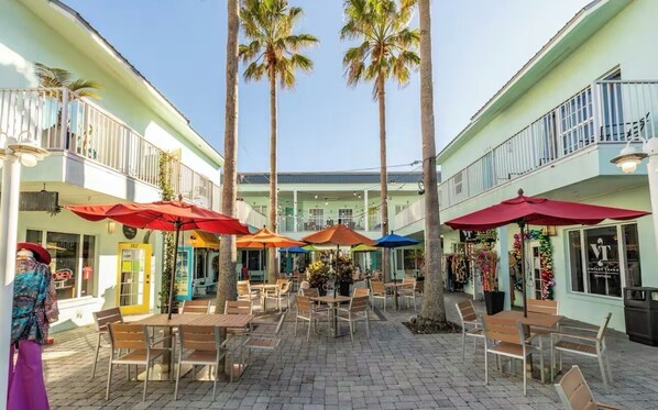 An outdoor patio area with tables and chairs, palm trees, and umbrellas.